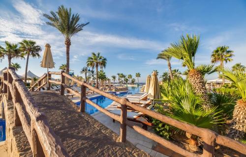 a wooden bridge leading to a pool with palm trees and umbrellas at Adams Beach Hotel & Spa in Ayia Napa