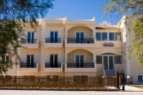 un grand bâtiment blanc avec des fenêtres bleues et une clôture dans l'établissement Garifalo Apartments, à Kalyves