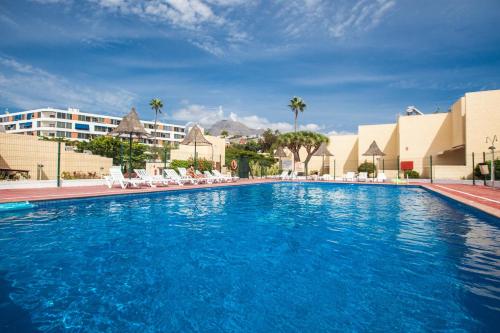una grande piscina blu con sedie e edifici bianchi di Cortijo a Playa de las Americas