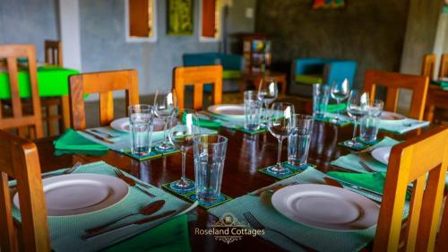 una mesa de madera con platos y vasos. en Roseland Cottages, en Bandarawela