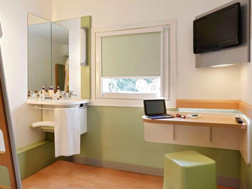 a bathroom with a laptop sitting on a counter with a window at IBIS Budget Aix en Provence Est Le Canet in Meyreuil
