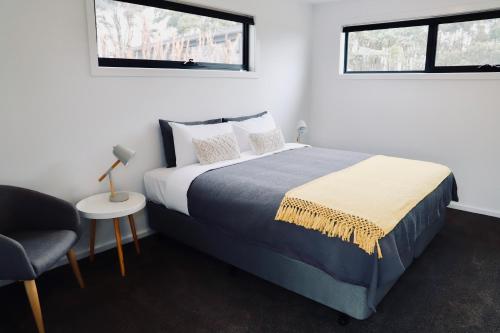 a bedroom with a bed and a chair and two windows at By Moonlight in Wattle Hill