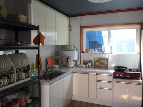 eine Küche mit weißen Schränken, einem Waschbecken und einem Fenster in der Unterkunft Jeju Guesthouse in Jeju-do