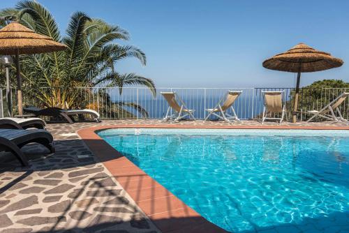 a swimming pool with chairs and umbrellas and the ocean at Hotel Villa Rita in Marciana