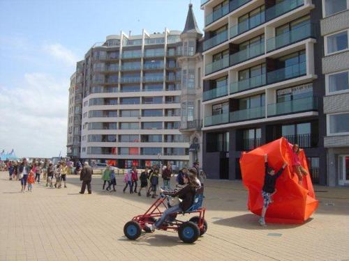 a woman riding a scooter with a large orange kite at Panoramic view on beach, ships, sea - place to be in Ostend