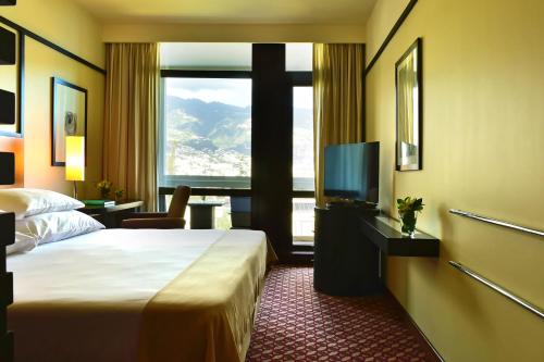 Cette chambre comprend un lit et une grande fenêtre. dans l'établissement Pestana Casino Park Hotel & Casino, à Funchal