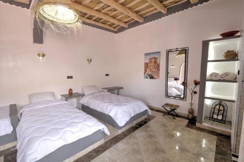 two beds in a white room with a mirror at Miguirne Chez Ali in Tamellalt