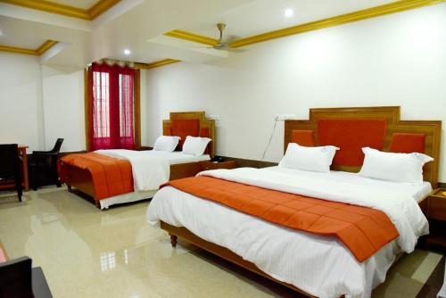 a bedroom with two beds with orange and white sheets at Hotel Chembiyan in Pudukkottai