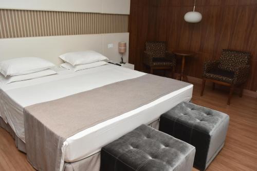 a bedroom with a large white bed and two chairs at Hotel Vilhar in Ivaiporã