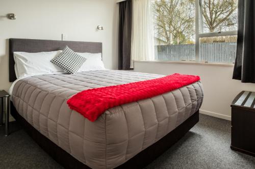 a bedroom with a large bed with a red blanket on it at Esplanade Motels in Gore