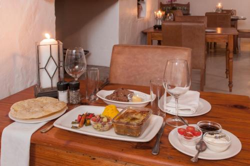 a wooden table with plates of food and wine glasses at Hotel Roosje van de Kaap in Swellendam