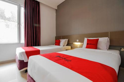 two beds in a hotel room with red pillows at RedDoorz near Goa Sunyaragi in Cirebon