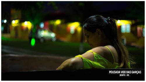 a young woman sitting on a bench at night at Pousada Voo das Garças in Bonito