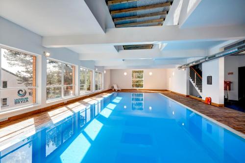 an indoor swimming pool with blue water and windows at Apartamenty Poddąbek- basen kryty, sauna, animacje dla dzieci , małpi gaj, baseny na dachu in Poddąbie