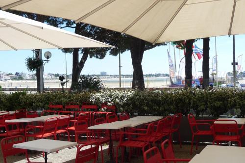 un restaurant avec des tables, des chaises rouges et des parasols dans l'établissement Le balcon de la Conche, à Royan