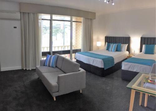 une chambre d'hôtel avec deux lits, un canapé et une chaise dans l'établissement Ensenada Motor Inn and Suites, à Adélaïde