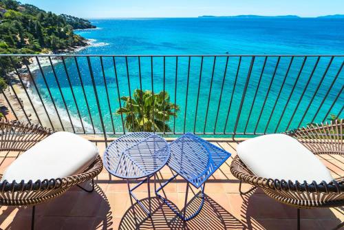 a balcony with chairs and tables and the ocean at Hôtel Le Bailli De Suffren in Rayol-Canadel-sur-Mer