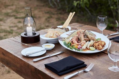 a wooden table with a plate of food and wine glasses at Jetwing Jungle Lodge, A Luxury Reserve in Yala