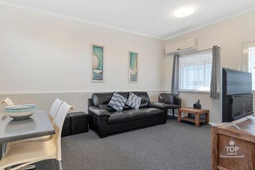 a living room with a black leather couch and a tv at Esperance Bay Holiday Park in Esperance