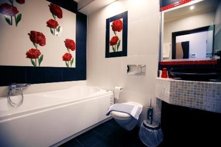 a bathroom with a white tub and red flowers on the wall at Dion Hotel in Paralia Katerinis