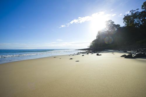a beach with the sun shining on the sand at Sofitel Noosa Pacific Resort in Noosa Heads
