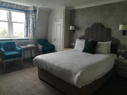 a hotel room with a bed and two blue chairs at voco The Clifton Folkestone by IHG in Folkestone