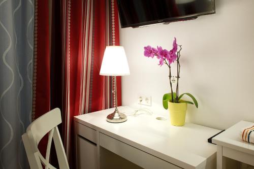 un escritorio blanco con una lámpara y una flor púrpura. en Pension am Wienfluss, en Viena