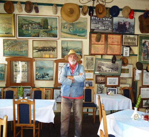 a man in a hat standing in a room with tables at Hotel Pelikan in Virpazar