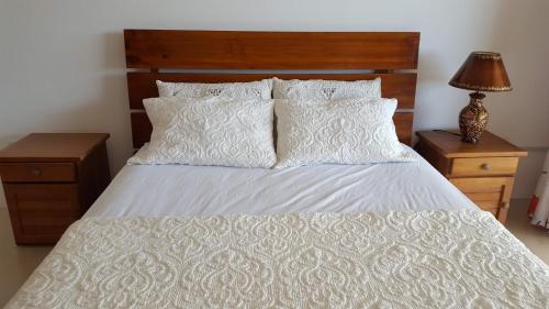 ein Schlafzimmer mit einem weißen Bett mit einem Kopfteil aus Holz und Kissen in der Unterkunft Mahina Luxury 2 Bedroom Apartment with Pool in Flic-en-Flac