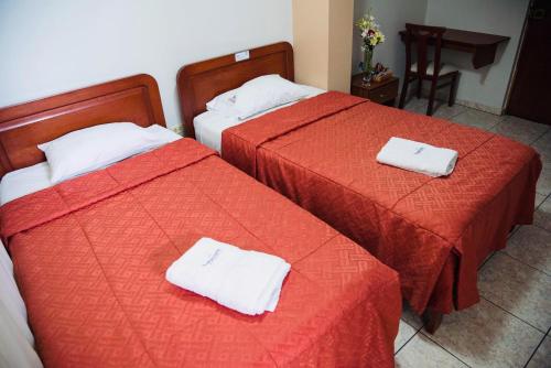 two beds with red sheets and white towels on them at Hotel Jorge Chavez in Trujillo