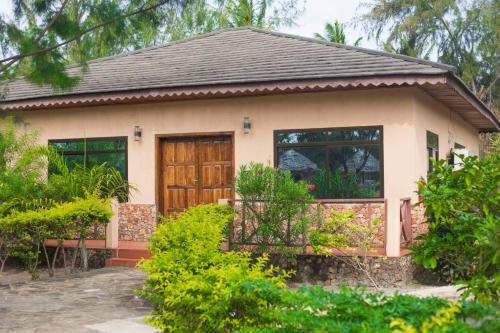 a small house with a brown door and some bushes at VRclub Paje Palms Beach Resort in Paje