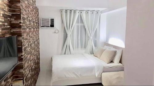 a white bedroom with a bed and a window at EV Place in Manila