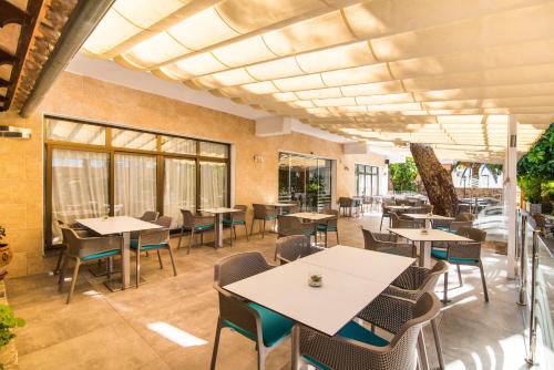 a restaurant with tables and chairs and windows at Hotel Baviera in Cala Ratjada