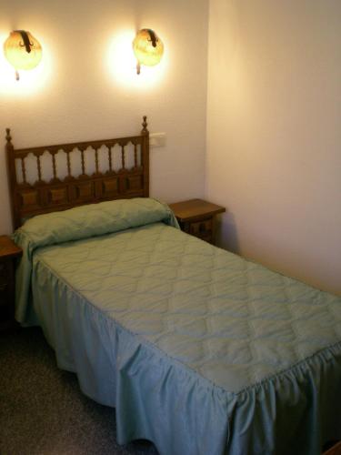 a bedroom with a bed with blue sheets and two tables at Hotel Puerta Romeros in Burgos
