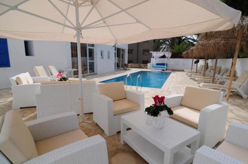 a patio with white chairs and an umbrella and a pool at Lithos Studios in Voroklini