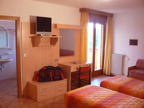 ein Hotelzimmer mit einem Bett und einem Schreibtisch mit einem TV in der Unterkunft Hotel & Appartamenti Al Larice in Ronzone