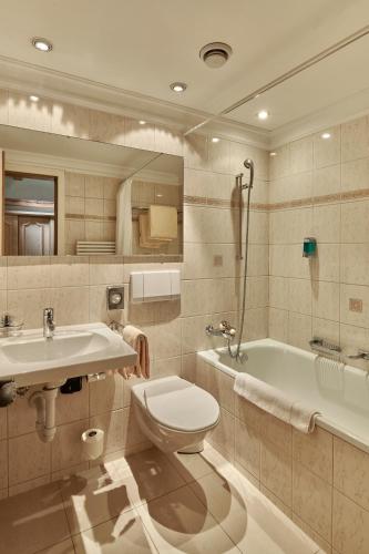 a bathroom with a toilet and a sink and a tub at Hotel Alphorn in Gstaad