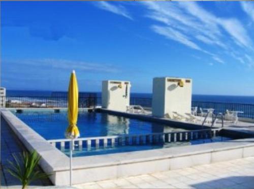 a swimming pool with a yellow umbrella and the ocean at Beach apartment... T1 with swimming pool (summer) in Costa da Caparica
