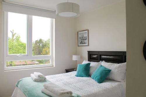 a bedroom with a bed with blue pillows and a window at Condominio Parque Almagro in Chillán