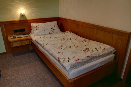 a bed with a wooden headboard and white sheets with red flowers at Pension Epple in Oberjoch