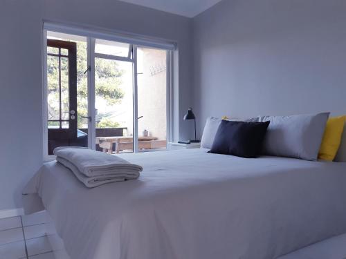 ein weißes Bett in einem weißen Zimmer mit Fenster in der Unterkunft Beautiful Bell Rock - partial inverter in Plettenberg Bay