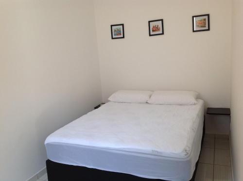 a small bedroom with a white bed with two pillows at Chalés Ubatuba 102 - P. Itaguá in Ubatuba
