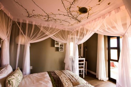 1 dormitorio con cama con dosel y cortinas blancas en Gondwana Kalahari Anib Lodge, en Hardap