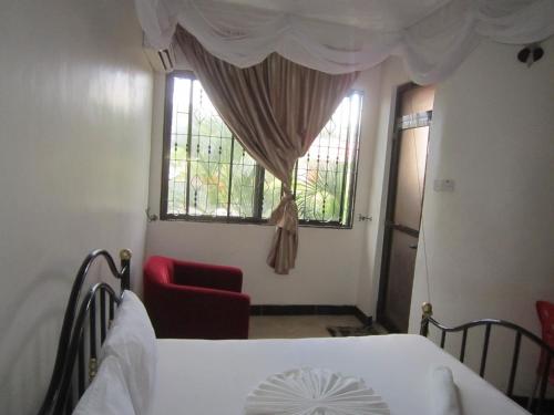 a bedroom with a bed and a window with a red chair at Jakicha Motel in Dar es Salaam