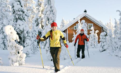 two people walking through the snow in front of a cabin at Santasport Apartment Hotel in Rovaniemi