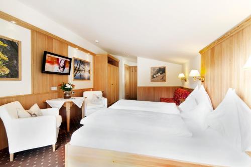 a hotel room with a large white bed and chairs at Landhotel Föhrenhof Ellmau in Ellmau