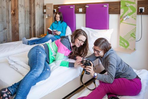 two girls laying on a bed with a camera at Explorer Hotel Hinterstoder in Hinterstoder