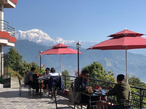 a group of people sitting at tables with red umbrellas at Hotel Pristine Himalaya in Pokhara