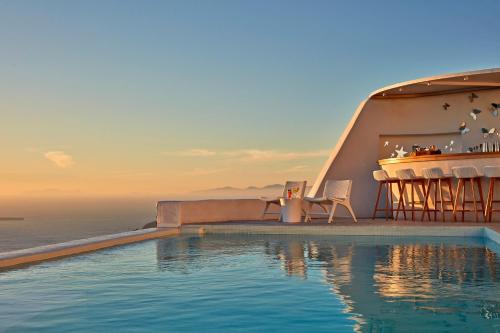 a swimming pool with a table and chairs next to the ocean at Astra Suites in Imerovigli