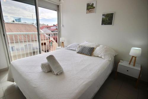 a bedroom with a white bed with a large window at Appartement Pomme Cannelle 1 chambre, moderne, au coeur de Fort de France in Fort-de-France